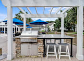 Thumbnail 28 of 42 - A white pergola with a grill and two chairs under it.
