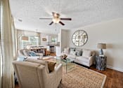 Thumbnail 6 of 42 - A living room with a beige couch, a glass coffee table, and a ceiling fan.