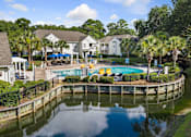 Thumbnail 1 of 42 - A pool surrounded by a fence and trees with houses in the background.