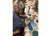 Thumbnail 53 of 57 - a woman sitting at a table working on a painting
