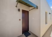 Thumbnail 6 of 11 - A white building with a brown door and a black mat in front.