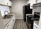 Thumbnail 9 of 11 - A black refrigerator sits in a kitchen with white cabinets and a granite countertop.