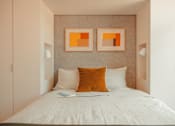 Thumbnail 10 of 36 - a small bedroom with a bed and two orange paintings on the wall at Scout Living, powered by Placemakr Apartments, Atlanta