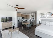 Thumbnail 9 of 23 - A modern bedroom with a bed, a table, a ceiling fan, and a kitchen area in the background at Anthem House Apartment , Huntsville, Alabama