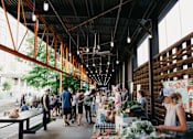 Thumbnail 31 of 36 - people shopping at a farmers market in a building with wooden beams at Scout Living, powered by Placemakr Apartments, Atlanta, GA, 30308