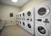 Thumbnail 22 of 39 - A row of white front load washing machines in a laundromat.