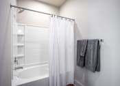 Thumbnail 32 of 39 - A white bathroom with a white tub and a white shower curtain.