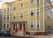 Thumbnail 2 of 14 - a yellow apartment building with a car parked in front of it