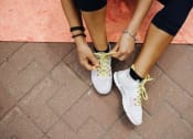 Thumbnail 19 of 42 - a woman tying her shoelaces on her sneakers