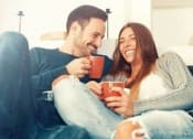Thumbnail 39 of 42 - a man and woman sitting on a couch holding cups of coffee
