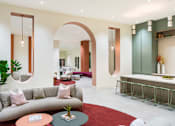 Thumbnail 11 of 25 - A modern living room with a grey sofa, a round table with a plant on it, and a red carpet.
