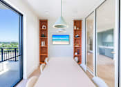 Thumbnail 14 of 25 - A modern room with a long white table and a television displaying a beach scene.