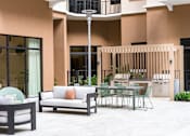 Thumbnail 24 of 25 - A patio with a white couch, a black table, and a glass table with chairs.