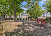 Thumbnail 5 of 40 - A playground with a red slide and a tree in the middle of a dirt area.