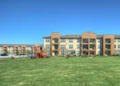 Thumbnail 19 of 28 - a large grassy area with a playground in front of a building at Retreat at Shadow Creek Ranch Apartments, Woodburn