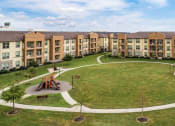 Thumbnail 9 of 28 - a park with a large grassy area and a playground in front of an apartment building at Retreat at Shadow Creek Ranch Apartments, Woodburn, TX