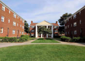Thumbnail 9 of 12 - a grassy area with a tree in the middle of it in front of two brick buildings at Parkland Village, Forestville, MD