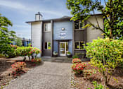Thumbnail 12 of 24 - the front of a grey building with a walkway and plants at Eagles Landing Apartments, Everett, 98204