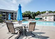 Thumbnail 22 of 43 - A table with two chairs and a blue umbrella sits by a pool.