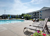 Thumbnail 19 of 43 - A pool area with lounge chairs and a building in the background.