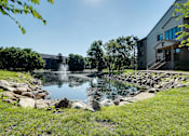 Thumbnail 5 of 43 - A fountain in the middle of a grassy area with a building in the background.
