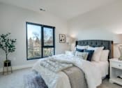 Thumbnail 6 of 18 - A bedroom with a large bed, a nightstand, and a window with a view of trees.