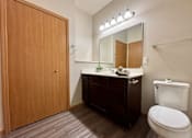 Thumbnail 29 of 34 - A bathroom with a wooden door, a white toilet, a mirror, and a vanity with a plant on top.