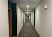 Thumbnail 13 of 34 - A long hallway with a carpeted floor and a door on the left.