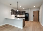 Thumbnail 9 of 18 - A modern kitchen with a wooden floor and a white countertop.