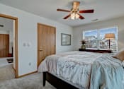 Thumbnail 36 of 44 - A bedroom with a bed, a ceiling fan, and a window overlooking a house.