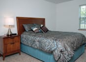 Thumbnail 35 of 44 - A bed with a wooden headboard and a blue comforter with a pattern on it.