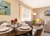 Thumbnail 39 of 43 - A dining table set with plates and glasses is in the foreground of a living room with a couch and television.