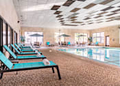 Thumbnail 11 of 43 - A large indoor swimming pool with lounge chairs and umbrellas.