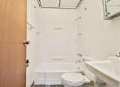 Thumbnail 10 of 11 - A white toilet sits next to a white bathtub in a small bathroom.