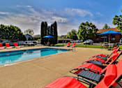 Thumbnail 2 of 33 - A pool surrounded by red chairs and a blue umbrella.