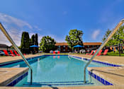 Thumbnail 1 of 33 - A swimming pool with a blue sky and trees in the background.