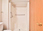 Thumbnail 31 of 33 - A white bathroom with a toilet, a shower, and a wooden door.