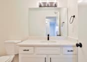 Thumbnail 29 of 33 - A white bathroom with a sink, toilet, and mirror.