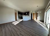 Thumbnail 17 of 34 - A spacious room with wooden flooring and a kitchen area in the background.