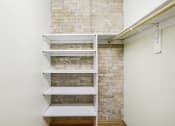 Thumbnail 14 of 35 - a walk in closet with white shelves and brick walls
