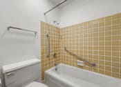 Thumbnail 51 of 52 - A white toilet sits next to a white bathtub in a bathroom with yellow tiles.