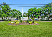 Thumbnail 17 of 52 - A sign in a grassy area with trees and a blue sky in the background.