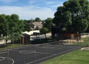 Thumbnail 33 of 33 - A basketball court is surrounded by a fence and there are houses in the background.