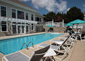 Thumbnail 12 of 44 - A pool with chairs and umbrellas in front of a house.