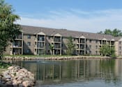 Thumbnail 2 of 43 - A building with a grey roof and a pond in front.