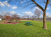 Thumbnail 4 of 48 - A playground with a green picnic table and a wooden swing set.