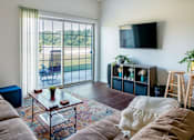 Thumbnail 57 of 60 - A living room with a couch, a coffee table, a TV, and a window with a view of the outside.