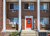 Thumbnail 7 of 27 - A red door is the centerpiece of a brick building with white columns.
