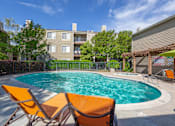 Thumbnail 10 of 37 - Resort-style swimming pool at Caifornia Place in gated pool area surrounded by lush greenery and blue skies for a beautiful and relaxing poolside experience. With plenty of seating including dining tables and chaise lounges