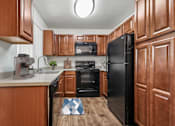 Thumbnail 21 of 31 - Kitchen in 2 Bed 1 Bath Bent Tree Apartment home with wood-style plank flooring, cherry wood cabinets, black appliances, and plenty of storage space for all of your needs!